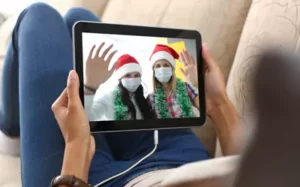 Tablet displaying a video call with two masked people in Santa hats waving during a virtual greeting
