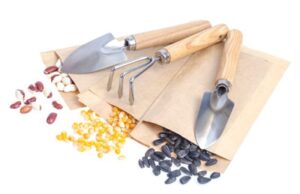 Gardening hand tools with wooden handles placed beside assorted seeds on paper packaging