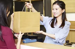 Person handing a brown paper shopping bag across a retail counter during a purchase