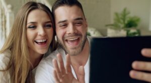 Two people sitting together and waving at a tablet during a video call