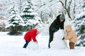Children and an adult building snowmen together in a snowy winter landscape