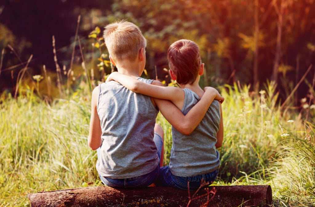 Children sitting on a log outdoors symbolize friendship and togetherness
