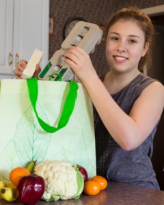 Person placing an egg carton into a reusable green shopping bag