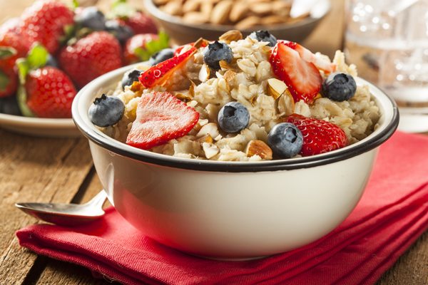 A bowl of oatmeal is placed on a red napkin with fresh fruit in the background