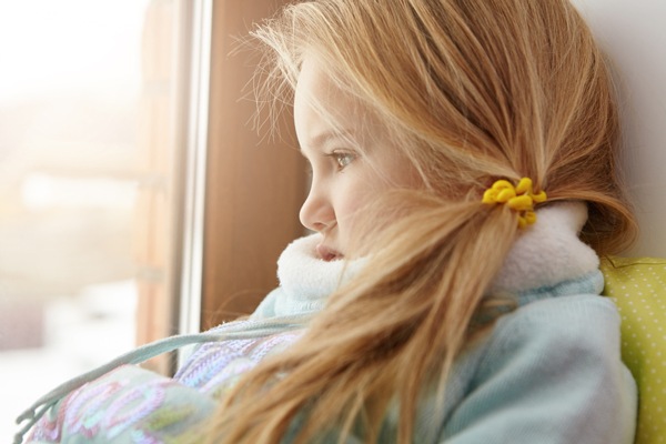 A child with blonde hair sitting by a window and looking outside on a quiet winter day