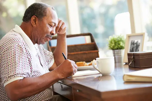 A person writing in a notebook with a pen on a wooden desk