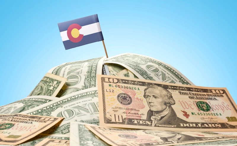 A Colorado flag sticking out of a pile of money by Century Support Services