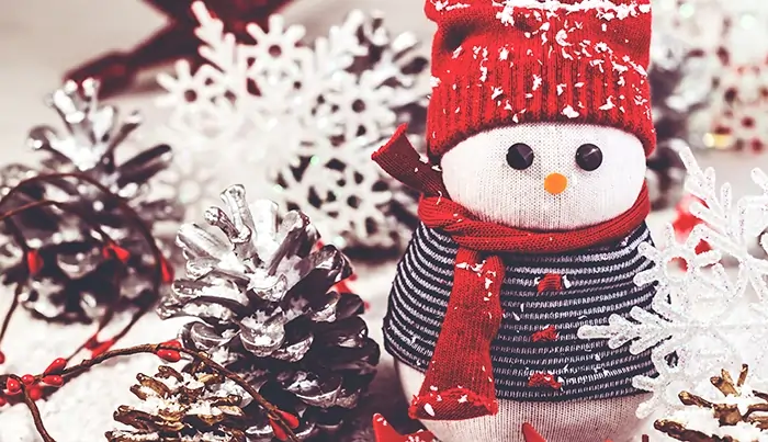 Snowman decoration with red hat and scarf surrounded by frosted pinecones and snowflakes
