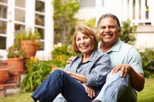 Two people sitting together on the grass in a garden area outside a home with plants

