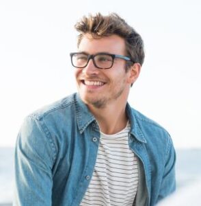 Person in a denim shirt and striped tee sitting outdoors near a bright seaside background