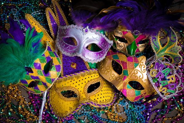 Colorful Mardi Gras masks with feathers and glitter displayed on beads in vibrant colors