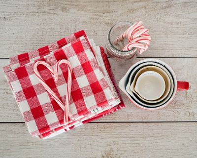 Candy canes on checkered napkins beside a mug with nested cups and a jar of candy canes