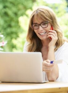 Person using a laptop outdoors while holding a credit card and talking on the phone