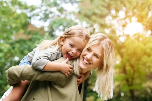 Person giving a child a piggyback ride outdoors with trees and sunlight behind them