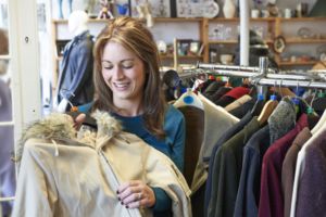Person shopping in a clothing store while holding up a light-colored coat near a rack