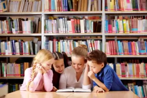 Children sitting at a library table reading an open book together