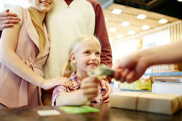 Child handing money to a cashier while adults stand nearby during a purchase
