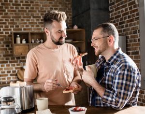 Two people preparing food together in a brick‑walled kitchen with a toaster and jars