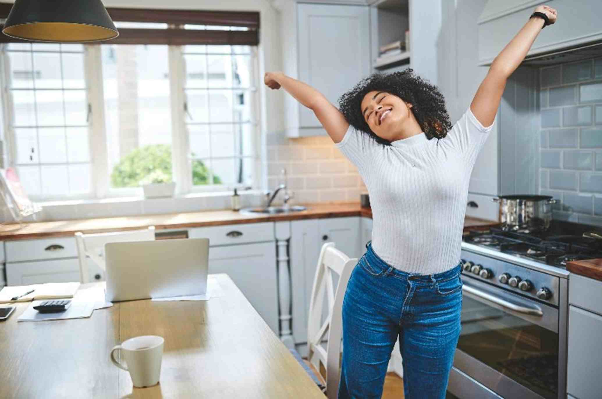 Person stretching with arms raised near a kitchen table holding a laptop