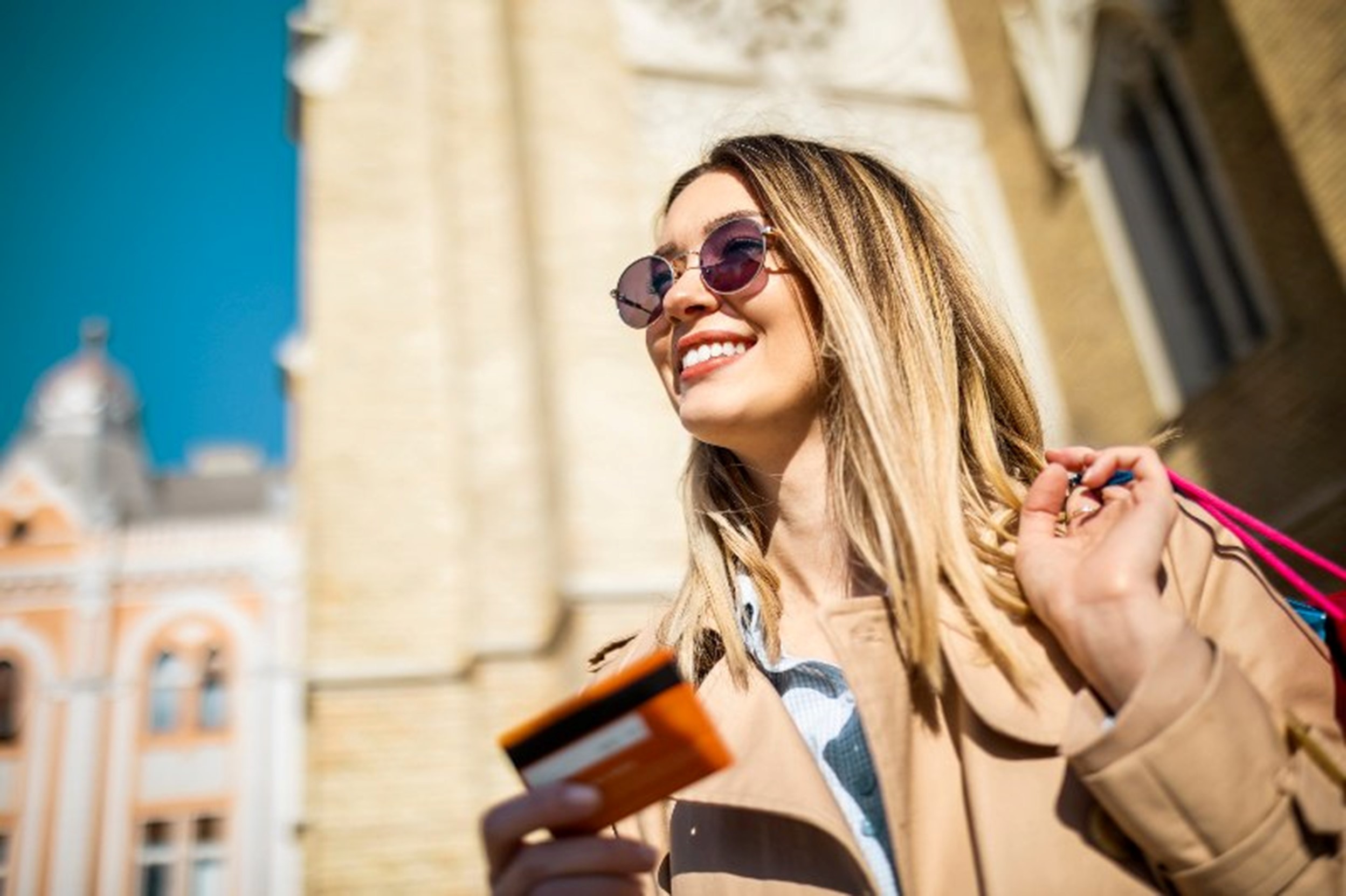A woman smiling while holding a credit card in front of a building by Century Support Services