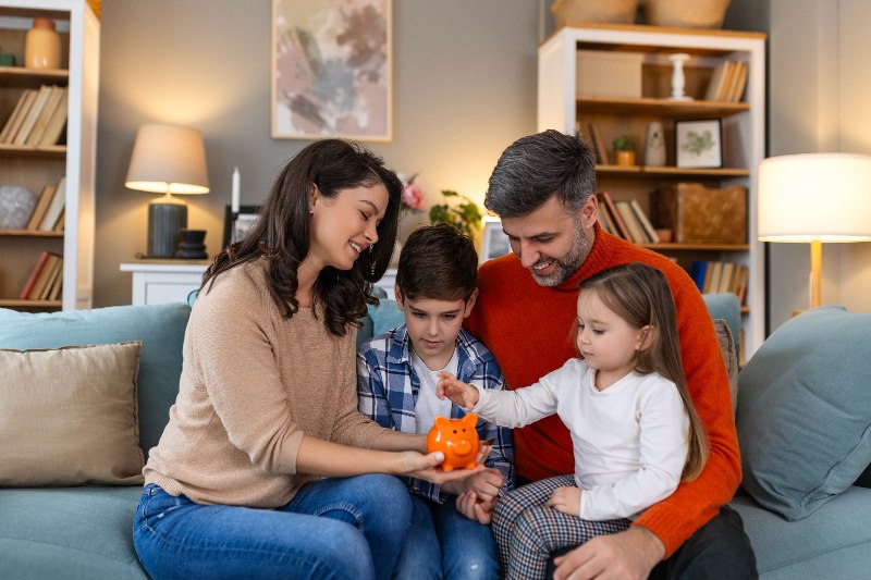 A family holding a piggy bank and putting money in it by Century Support Services