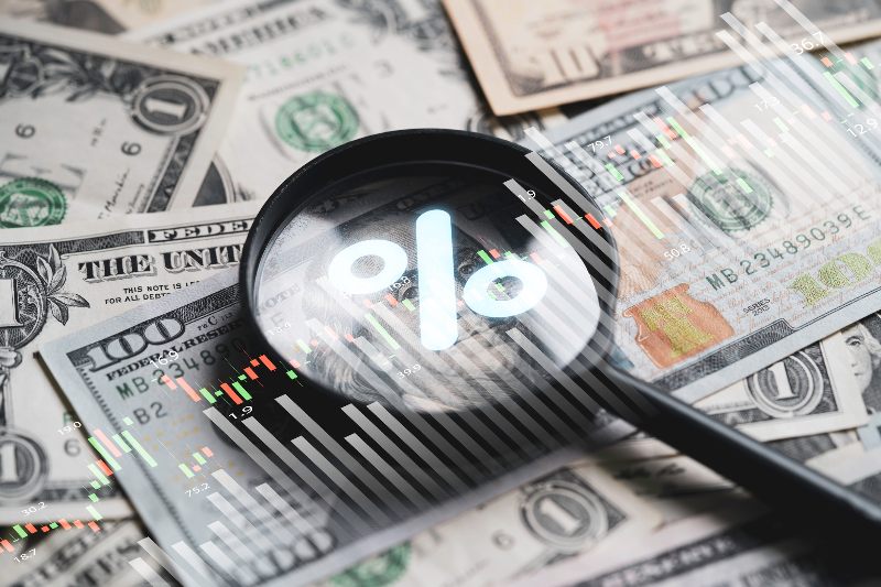 Money with a magnifying glass and percentage symbol on top by Century Support Services