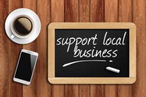 Chalkboard reading support local business beside a coffee cup and smartphone on a wooden table
