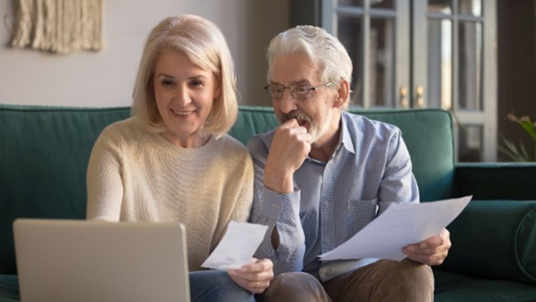 A senior couple smiling while looking at a laptop and papers by Century Support Services